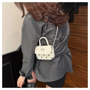 Polka dot mini square bag with silver bow buckle worn as a crossbody on a shoulder