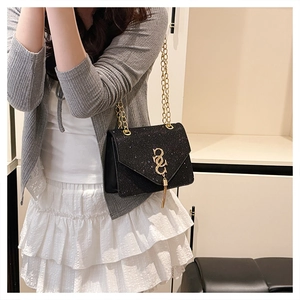 Close-up of black glitter crossbody bag with gold tassel buckle and chain on model