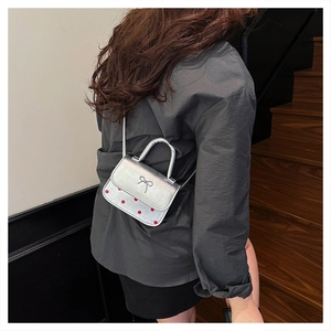 Detail of silver crossbody bag with red polka dots and bow accent on a mini square purse