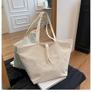 Detail of off-white canvas tote bag featuring premium embroidery and durable texture