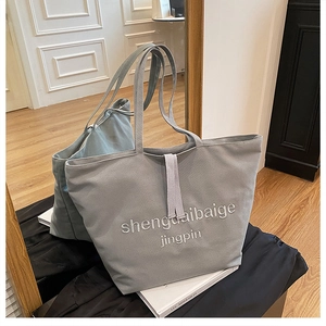 Detail of grey canvas tote bag featuring embroidered text and textured fabric finish