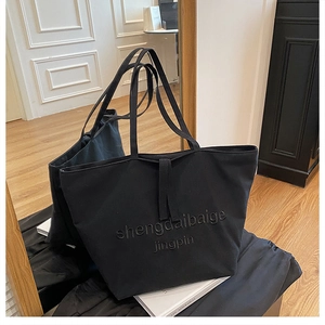Detailed view of black canvas tote bag with embossed letters on a wooden floor
