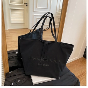 Detail shot of a large black tote bag featuring embossed lettering and long shoulder straps