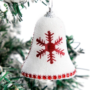 White foam Christmas bell with red snowflake on a snowy pine branch ornament