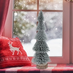 Mini flocked Christmas tree with natural wood base on a cozy winter windowsill