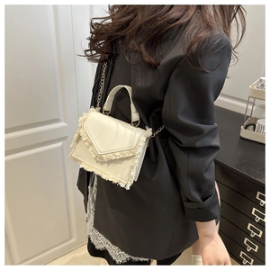 Chic white crossbody bag with fringe detailing and gold chain strap on model