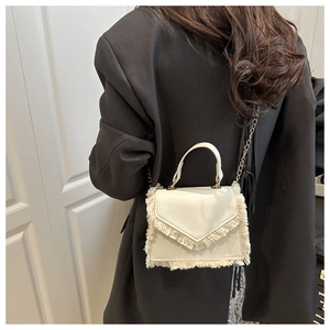 Detail of a chic cream square handbag featuring elegant fringe trim and a gold chain strap