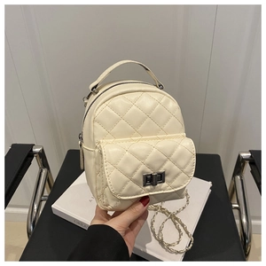 Detail of cream quilted mini backpack with silver twist lock and chain strap on books