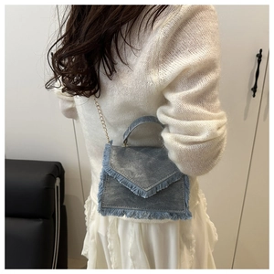 Detail view of denim mini bag featuring fringe edges and golden chain strap for crossbody wear