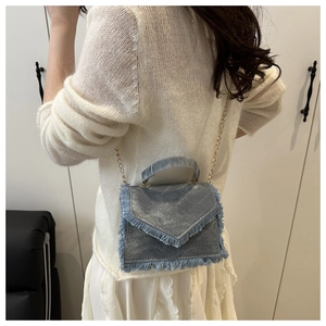Close-up of a blue denim crossbody bag with fringe details and a gold chain strap
