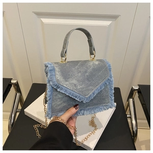 Detail of light blue denim handbag with frayed fringe edges and gold chain strap