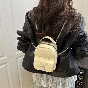 Chic beige quilted mini backpack with chain strap shown on model in stylish black jacket