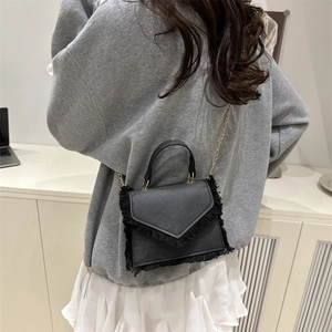 Chic black square bag with fringe details and gold chain strap shown on a model