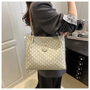 Detail of beige tote bag with M-pattern print and gold chain strap on model's shoulder