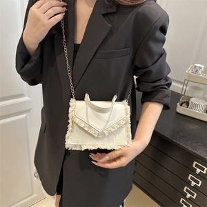 White fringe flap crossbody bag with gold chain strap worn over a black blazer