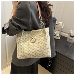 Detail of a beige tote bag with black M pattern and gold metal logo on a model