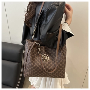 Close-up of brown monogram tote bag featuring gold M-pendant and leather strap detail