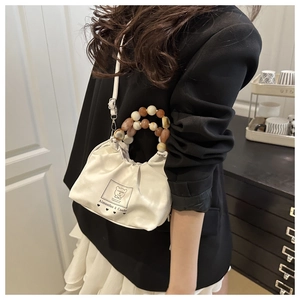 Close-up of a white pleated bucket bag with amber resin bead handle and bear logo detail