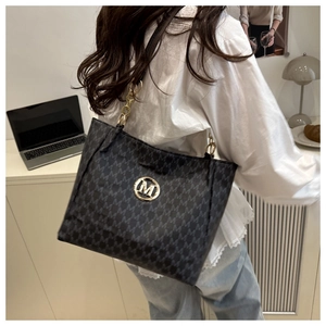 Close-up of a grey tote bag featuring M monogram pattern and a gold circular logo buckle