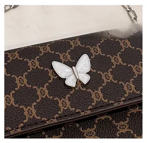 Detailed macro view of dark brown crossbody bag with embossed patterns and butterfly clasp