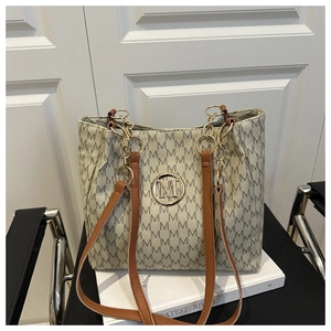 Detail of cream tote bag featuring grey M-letter print and golden metallic logo emblem