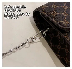 Detail of detachable gold chain strap on brown monogrammed crossbody bag for women