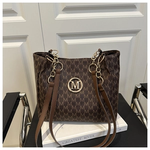 Detail of brown monogram tote bag with gold M logo and chain strap on a white stand