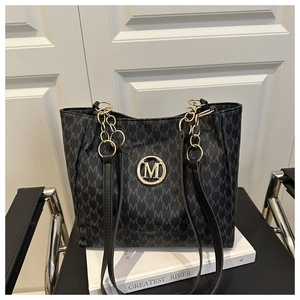 Detail of black monogram tote bag with gold M logo on a white book and black chair