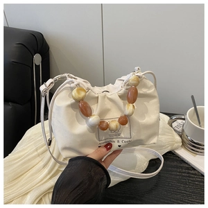 Detail of cream drawstring bucket bag with amber beaded handle and brand logo