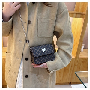 Detail of a brown monogram crossbody bag with a silver butterfly ornament and metal chain