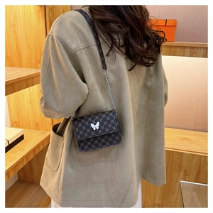 Detail of a brown monogram crossbody bag with a white butterfly ornament on the flap