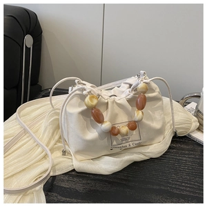 Detail of cream canvas bucket bag featuring colorful beaded handle and drawstring strap