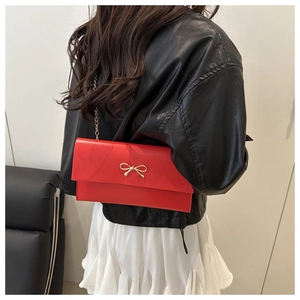 Detail of red envelope crossbody bag with gold bow ornament and metal chain strap