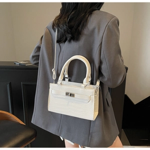 Detail of white crocodile pattern handbag with silver lock worn with grey suit