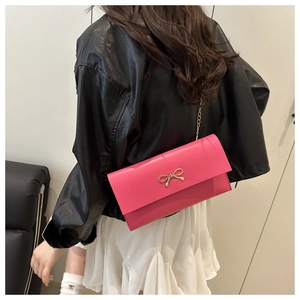 Detail of rose red flap crossbody bag with golden metal bow clasp and fine chain strap
