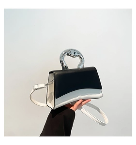 Detail of a color-block leather handbag featuring a unique silver fluid-shaped metal handle