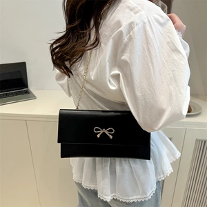 Minimalist black square crossbody bag with gold bow clasp and elegant chain strap