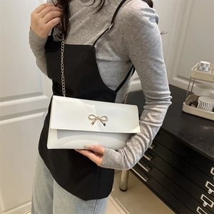 Elegant white crossbody bag with gold bow buckle and chain strap on a female model