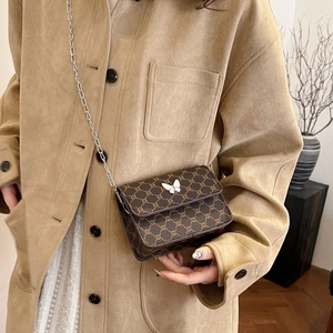 Brown monogram crossbody bag with white butterfly buckle and silver chain on suede coat