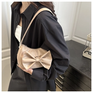Close-up of beige moon-shaped shoulder bag featuring a large decorative bow and thin strap