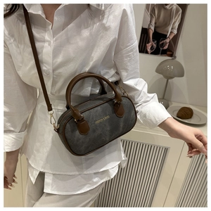 Detail of dark grey cylinder bag with brown leather handles and golden fashion text