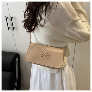 Shoulder view of a beige minimalist small square bag with a golden bow buckle detail
