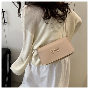 Close-up of beige shoulder bag with golden bow clasp worn by model in a minimalist setting