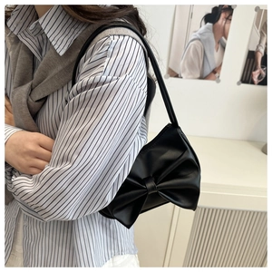 Detail of a chic black shoulder bag featuring a large decorative bow and leather texture