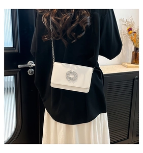 Close-up of white square crossbody bag featuring a large silver rhinestone buckle and chain