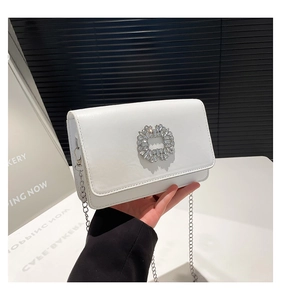 Close-up of a white leather flap bag featuring a sparkling rhinestone buckle and chain strap