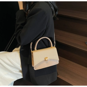 Détails d'un sac beige avec poignée dorée présenté sur un escalier en bois brun