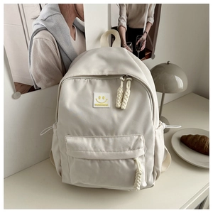Detail of cream nylon backpack with smiley face patch and braided rope zippers