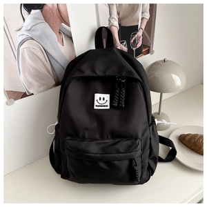 Detailed view of black nylon backpack with smiley patch, front pocket and side bottle holders