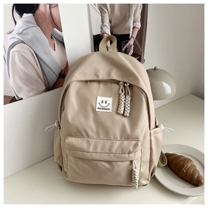 Detail of beige nylon backpack featuring smiley patch and woven rope zipper pulls